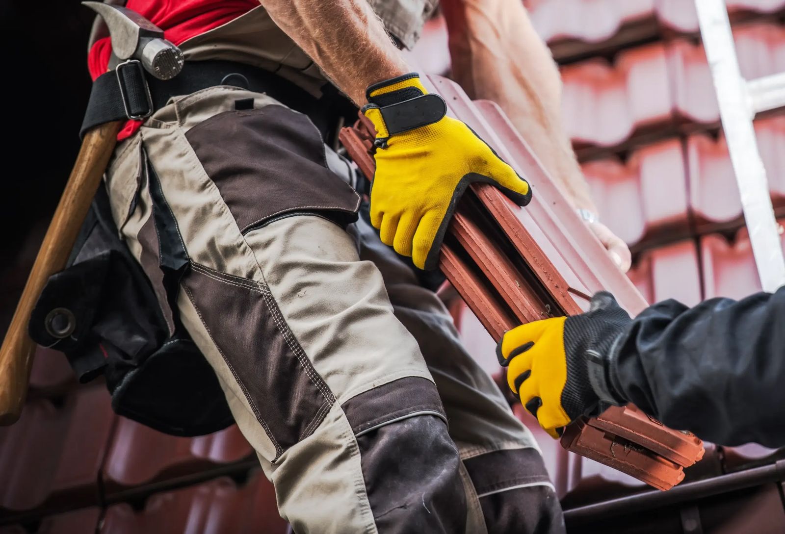 Roofer carrying clay roof tiles up a ladder onto a tiled roof