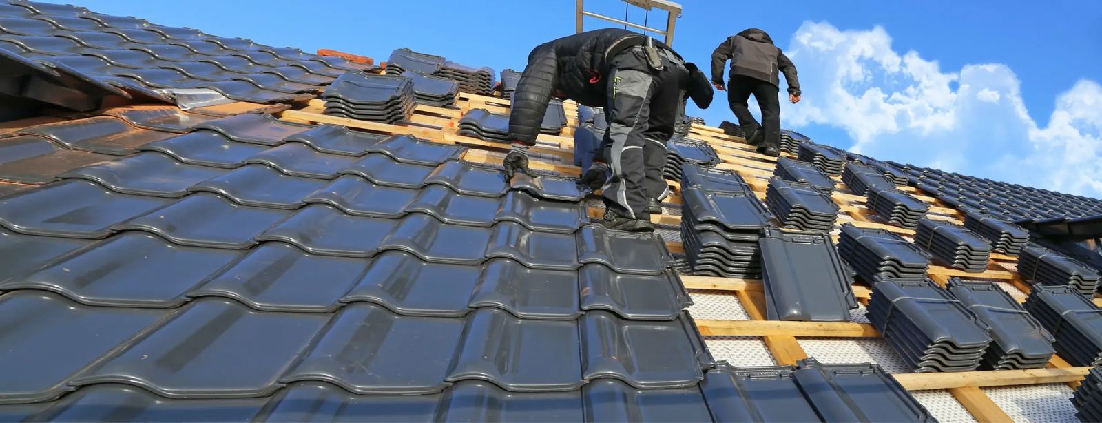 Two roofers laying interlocking concrete tiles on a re-roofed house